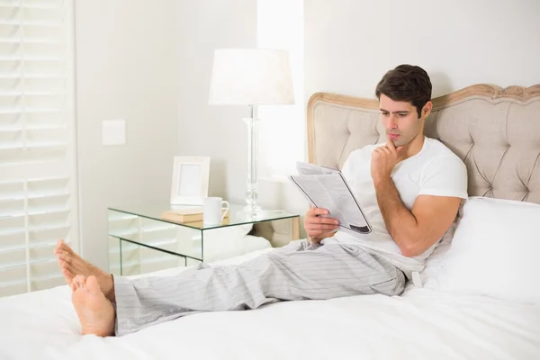 Casual man reading newspaper in bed — Stock Photo, Image