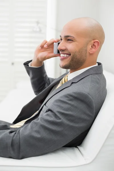 Uśmiechający się elegancki biznesmen za pomocą telefonów komórkowych na kanapie w domu — Zdjęcie stockowe