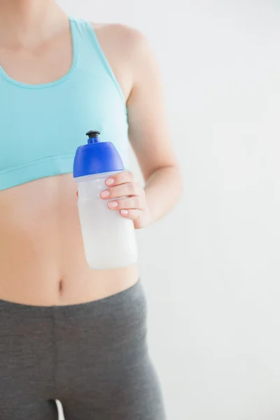 Mid section of fit woman holding water bottle against wall — Stock Photo, Image