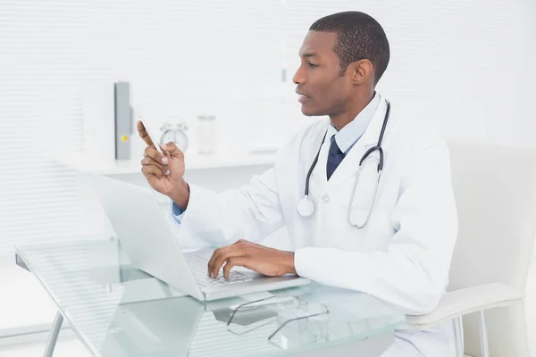 Doctor text messaging while using laptop at medical office — Stock Photo, Image