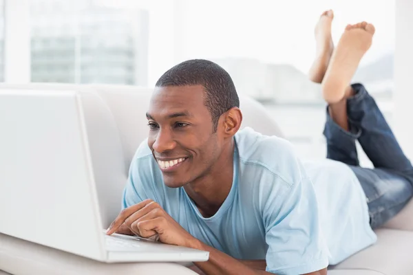 Relaxed casual Afro man with laptop lying on sofa — Stock Photo, Image