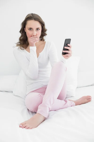 Shocked woman with mobile phone in bed — Stock Photo, Image