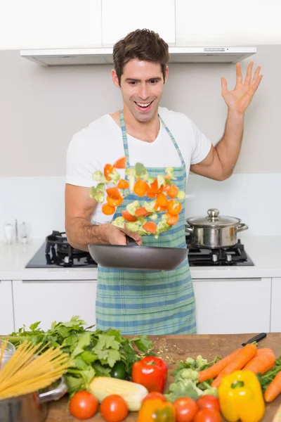 Cheerful man tossing vegetables in kitchen — Stock Photo, Image