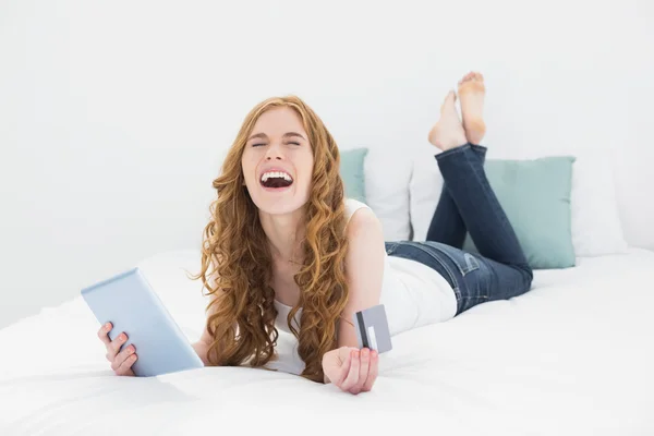 Chica pelirroja feliz con tablet PC y tarjeta de crédito en la cama — Foto de Stock