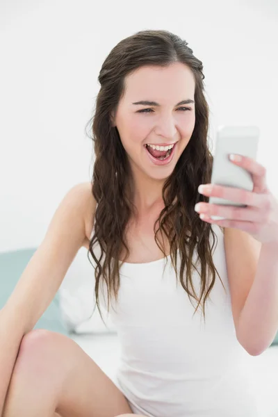 Veselá žena s mobilním telefonem v posteli — Stock fotografie