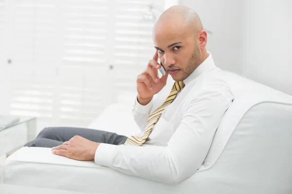 Uomo d'affari serio che utilizza il cellulare sul divano a casa — Foto Stock