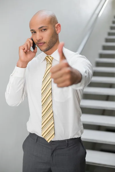 Biznesmen za pomocą telefonów komórkowych i gestykulacji kciuk w górę — Zdjęcie stockowe