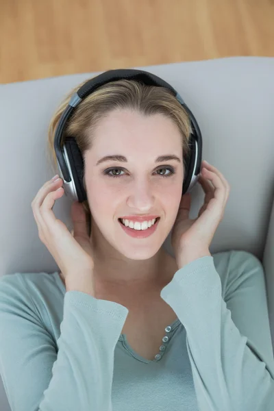 Hinreißende junge Frau, die mit Kopfhörern Musik hört und in die Kamera lächelt — Stockfoto