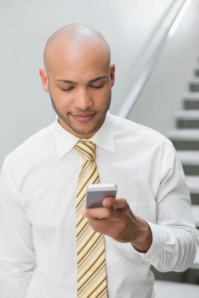 Smiling businessman text messaging against staircase — Stock Photo, Image