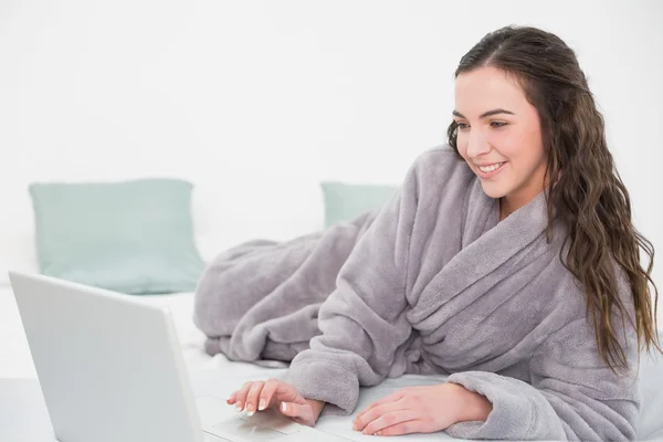 Morena en bata de baño usando laptop en la cama — Stockfoto