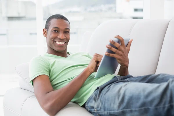 Casual smiling Afro man using digital tablet on sofa — Stock Photo, Image