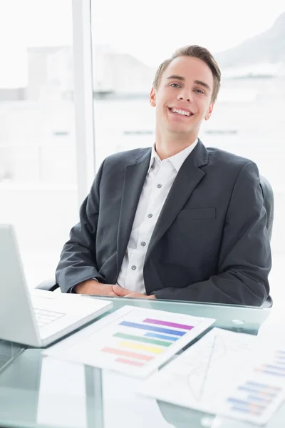 Sonriente joven hombre de negocios con portátil en el escritorio de la oficina —  Fotos de Stock