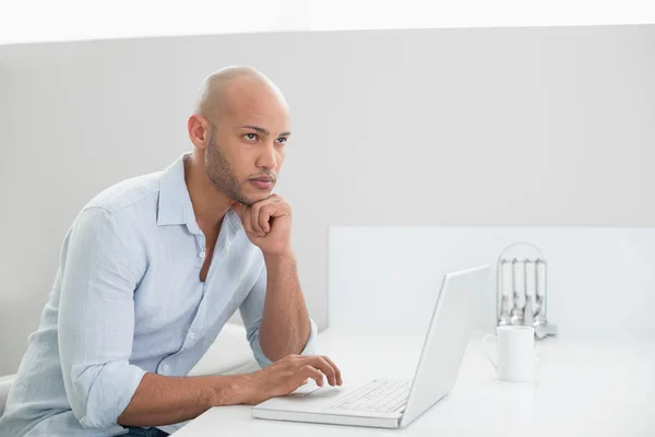 Pensativo hombre casual utilizando el ordenador portátil en casa —  Fotos de Stock