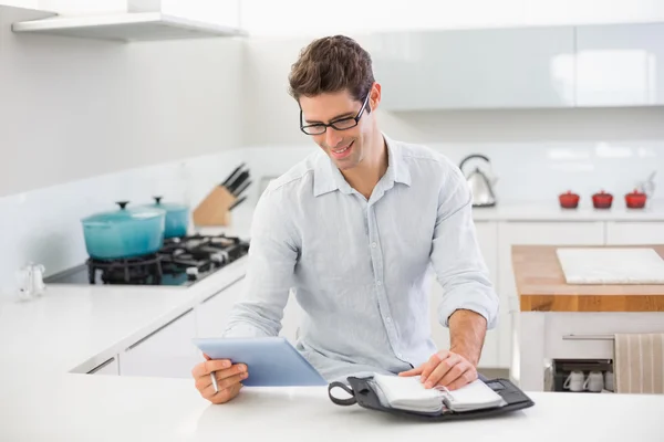 Glad avslappnad man med digital tablet och dagbok i köket — Stockfoto