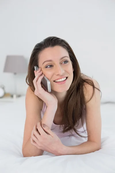 Mulher sorridente usando telefone celular na cama — Fotografia de Stock