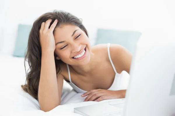 Sonriente mujer casual utilizando el ordenador portátil en la cama — Foto de Stock