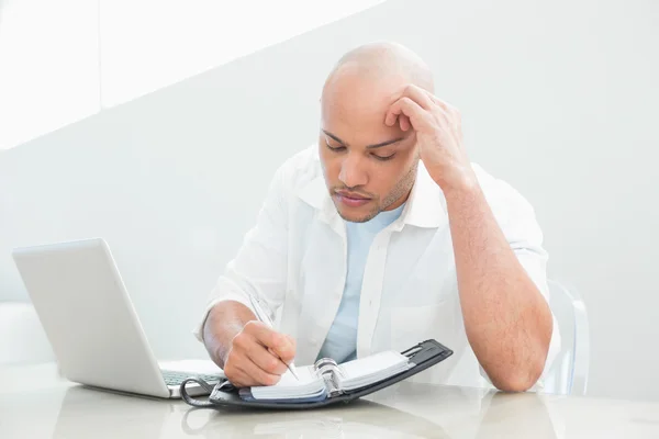 Casual ernstige man met laptop schrijven in dagboek — Stockfoto