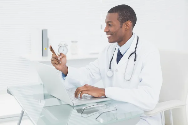 Mensagens de texto do médico masculino sorridente ao usar laptop — Fotografia de Stock