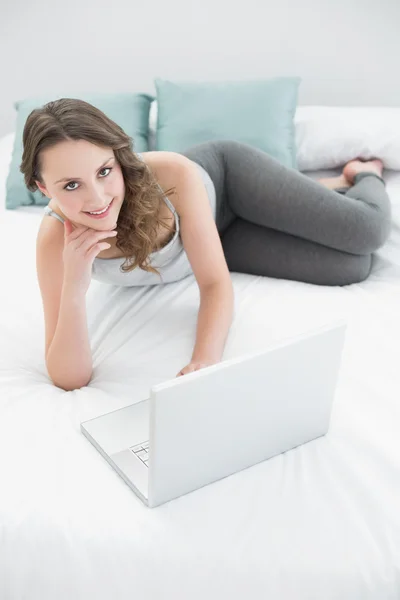 Sorridente casual giovane bruna con laptop a letto — Foto Stock