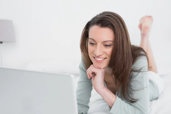 Relajada mujer sonriente casual utilizando el ordenador portátil en la cama — Foto de Stock