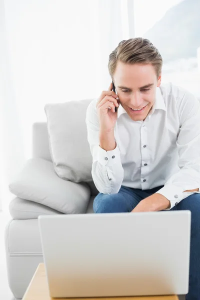 Jovem Casual usando celular e laptop no sofá — Fotografia de Stock