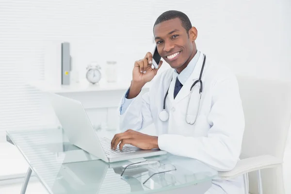 Mensagens de texto do médico masculino sorridente ao usar laptop — Fotografia de Stock