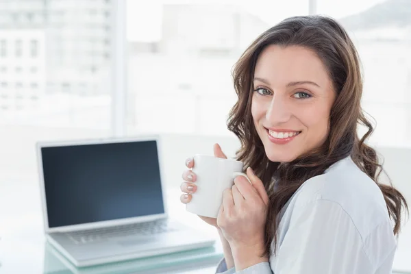 Donna d'affari con tazza di caffè davanti al computer portatile in ufficio — Foto Stock