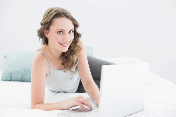 Sorridente bruna casual guardando il computer portatile a letto — Foto Stock