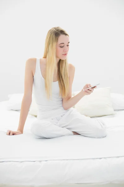 Content calm woman texting with her smartphone sitting on her bed — Stock Photo, Image