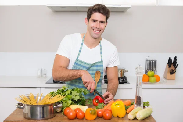 Sorrindo jovem cortando legumes na cozinha — Fotografia de Stock