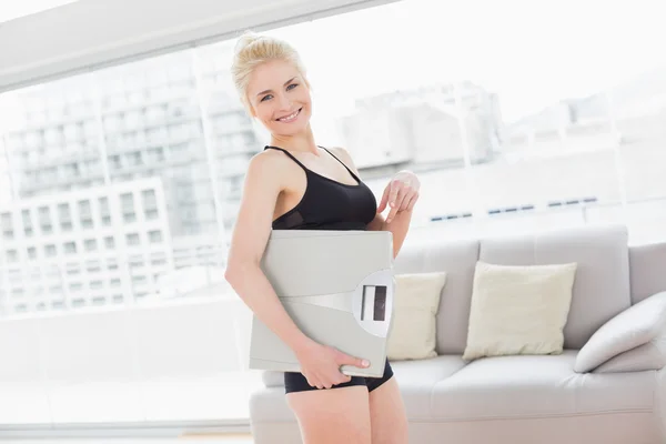 Woman in sportswear carrying scale in fitness studio — Stock Photo, Image