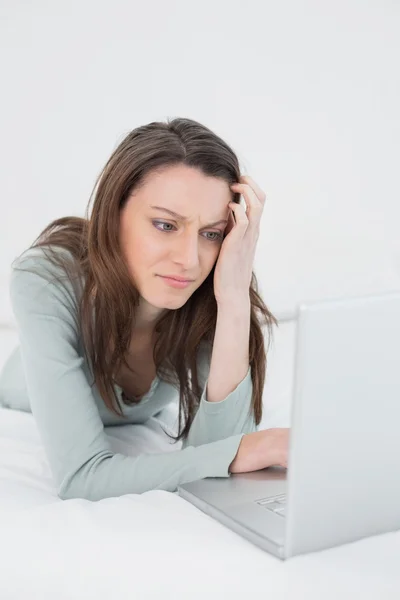 Mujer joven triste casual usando el ordenador portátil en la cama —  Fotos de Stock