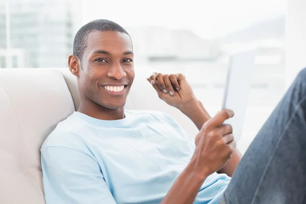 在沙发上使用数字平板电脑的黑人男人休闲微笑着 — 图库照片