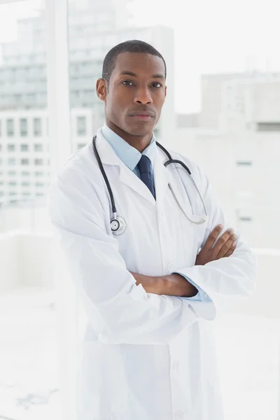 Médico serio con los brazos cruzados en un consultorio médico — Foto de Stock