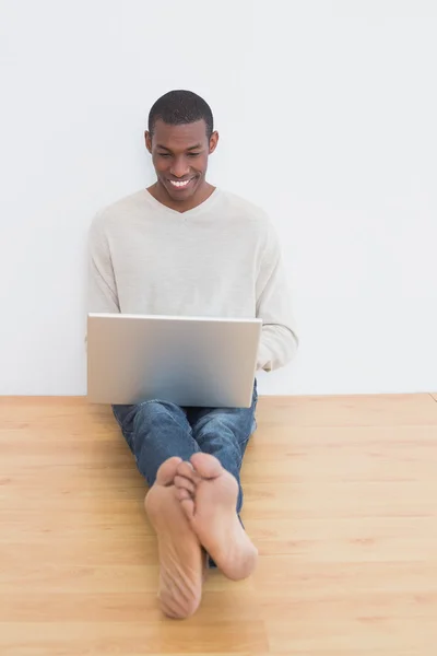 Gelukkig casual afro jonge man met behulp van laptop op verdieping — Stockfoto