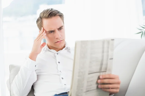 Portrait of a serious relaxed man reading newspaper on sofa — Stock Photo, Image