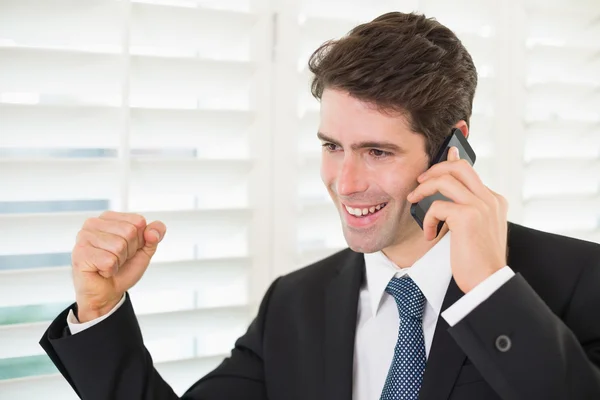 Empresário sorrindo usando telefone celular enquanto apertando o punho — Fotografia de Stock