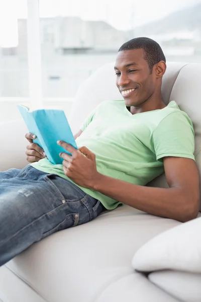Портрет улыбающегося афрочеловека, читающего книгу на диване — стоковое фото