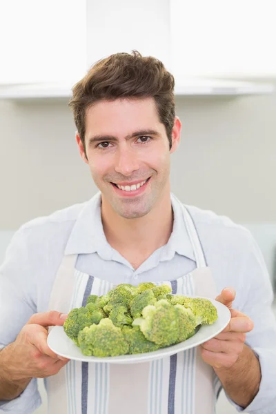 Sorrindo homem segurando uma placa de brócolis na cozinha — Fotografia de Stock