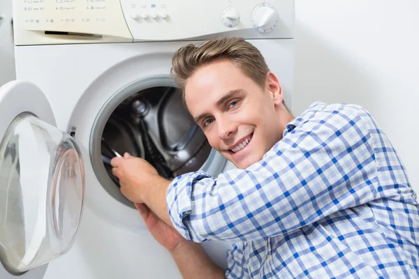 Técnico sorridente reparando uma máquina de lavar roupa — Fotografia de Stock