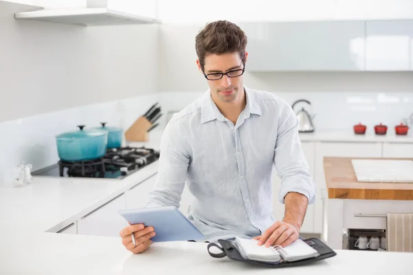 Cheerful casual man with digital tablet and diary in kitchen — Stock Photo, Image