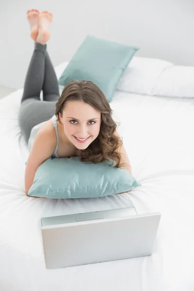 Casual brunette with laptop lying in bed — Stock Photo, Image