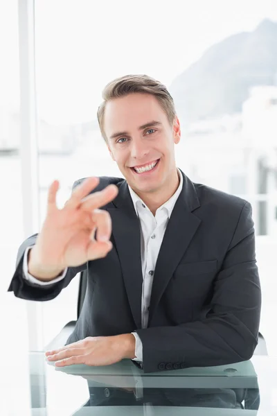 Smiling businessman gesturing okay sign at office desk — Stock Photo, Image