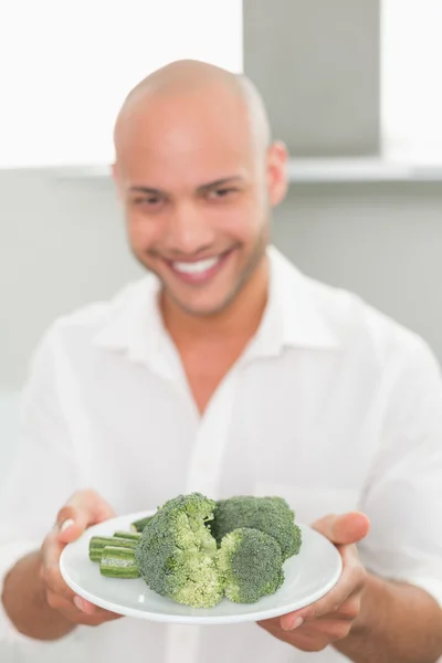 Sorrindo homem segurando uma placa de brócolis na cozinha — Fotografia de Stock