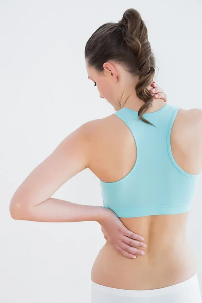 Vista trasera de una mujer tonificada con dolor de espalda contra la pared — Foto de Stock