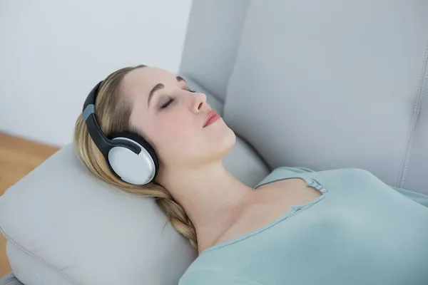 Casual blonde woman listening to music lying on couch — Stock Photo, Image