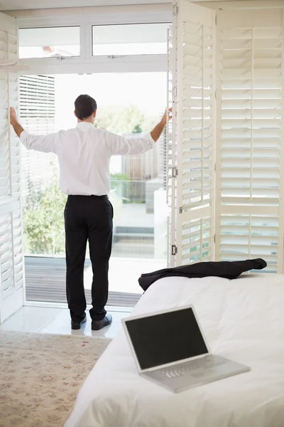 Businessman looking through window at a hotel bedroom — Stock Photo, Image