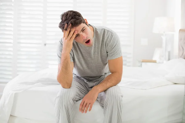 Schläfriger junger Mann sitzt und gähnt im Bett — Stockfoto