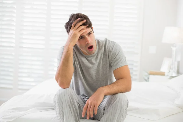 Schläfriger junger Mann sitzt und gähnt im Bett — Stockfoto