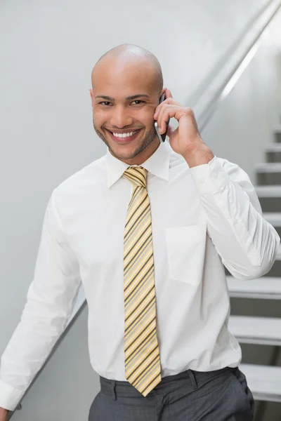 Smiling businessman using cellphone against staircase — Stock Photo, Image